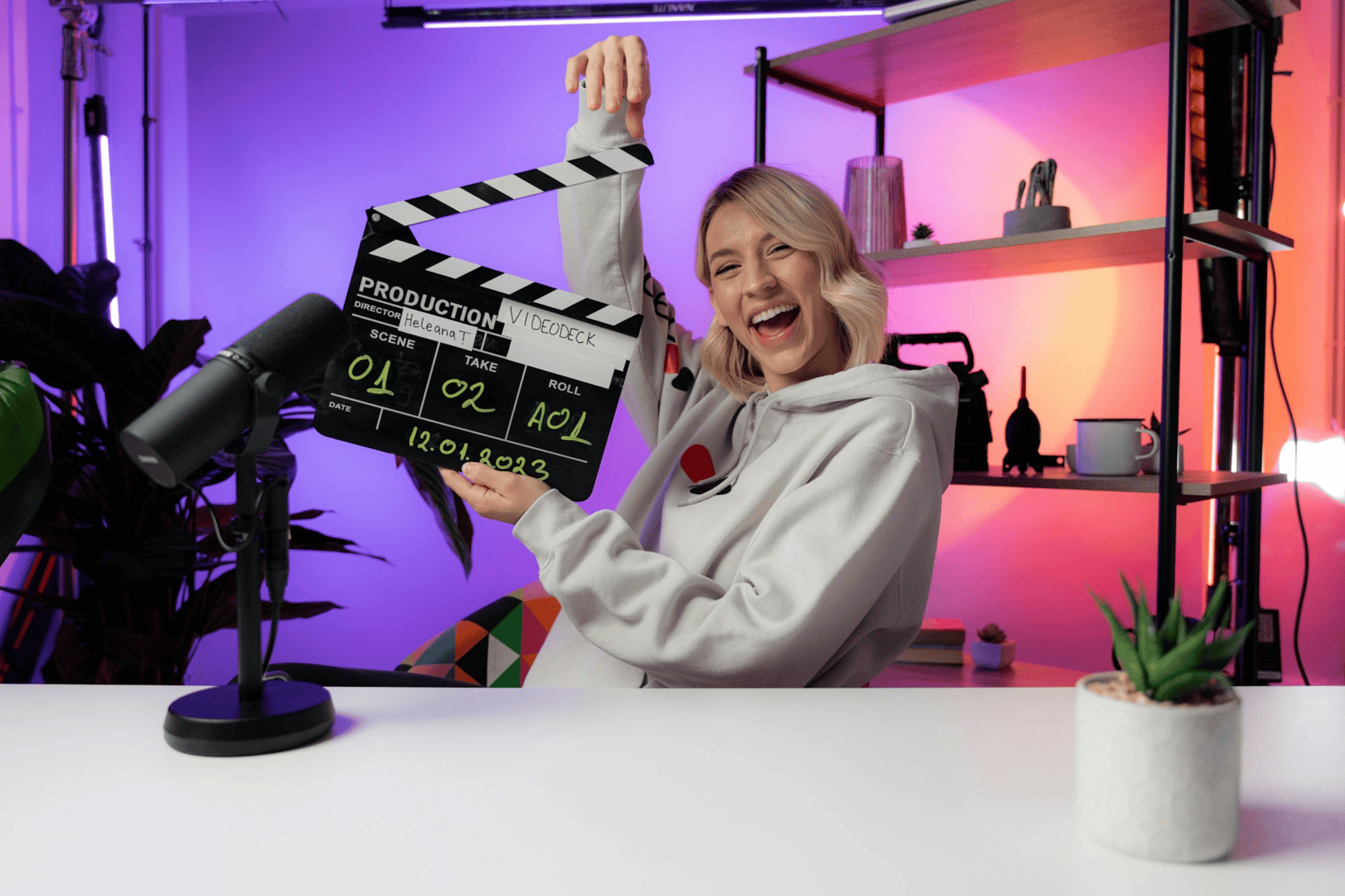 A happy video creator holding a production clapperboard in a colourful recording studio
